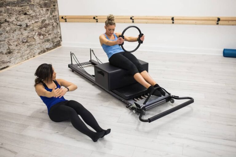 female trainer assisting woman with exercising with pilates ring